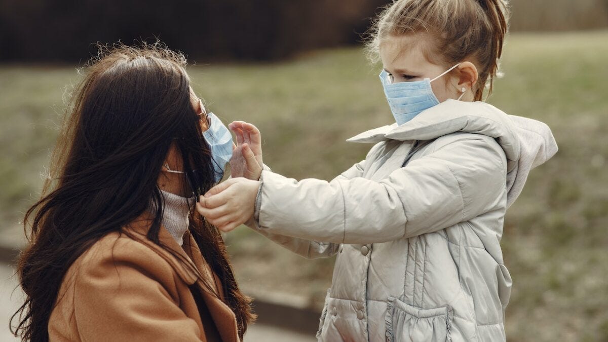 little girl touching her moms face while they are both wearing face masks
