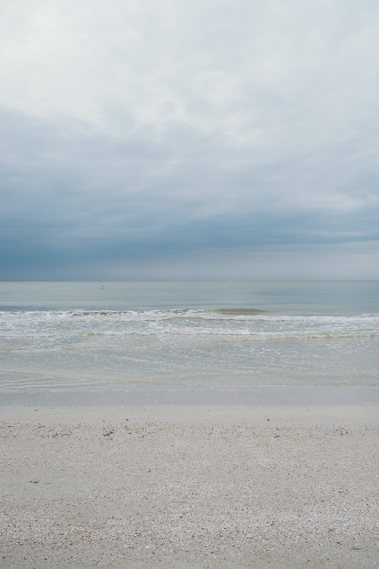 A view out to sea on a moody cloudy day. Gentle waves breaking on beach in foreground.