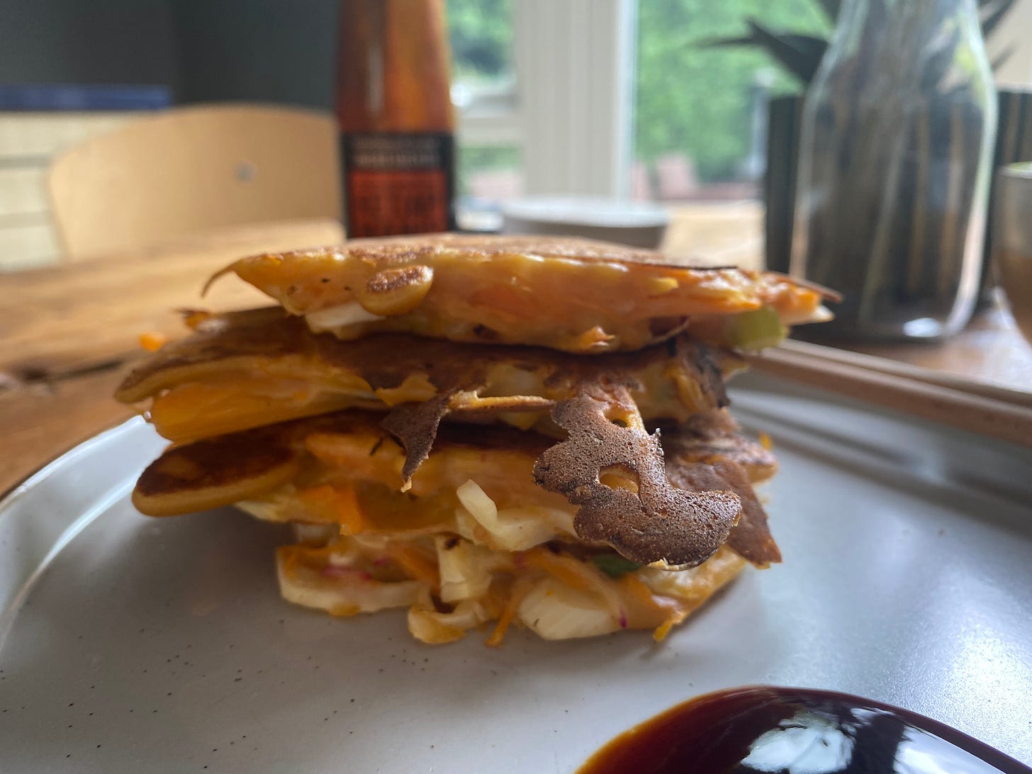 Stack of pancakes on a plate. A bottle of sauce is behind but out of focus