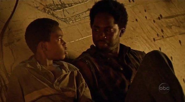 Walt Lloyd (Malcom David Kelley) and Michael (Harrold Perrineau) in a tent, looking at one another skeptically.