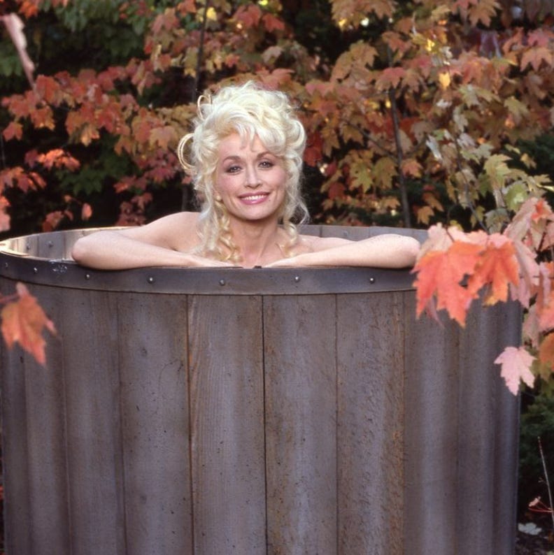 Dolly Parton in a hottub outside with autumn leaves surrounding her. festive