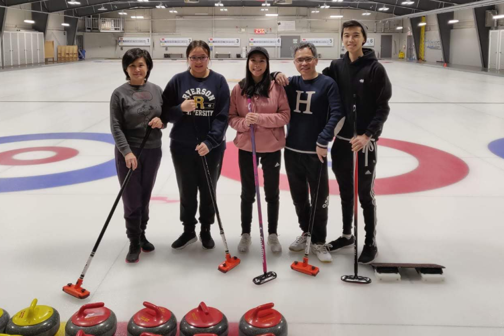 5 people standing on a curling rink smiling and posing.