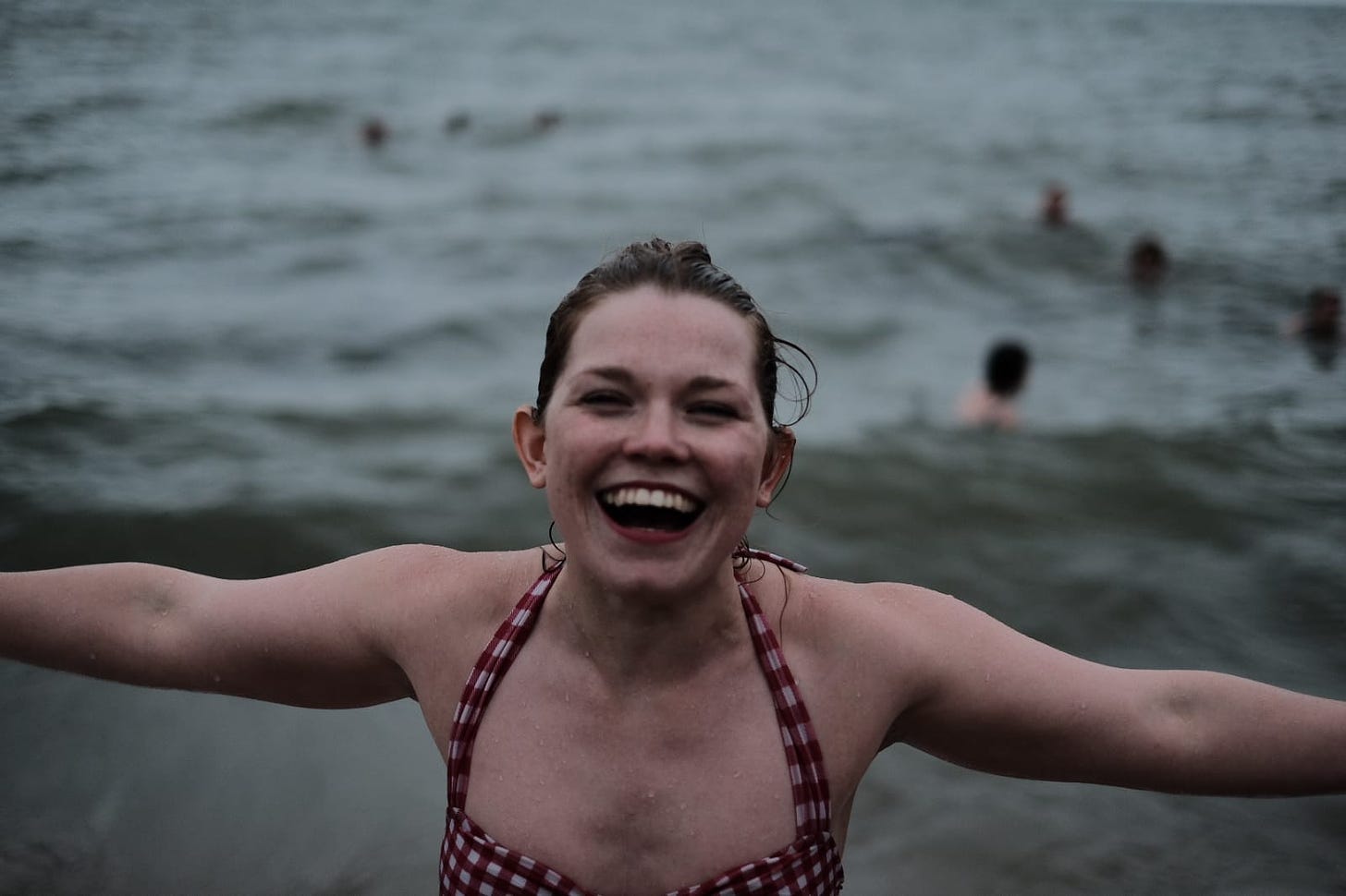 Libby walking out of the sea after a swim, arms wide open and with a big smile on her face