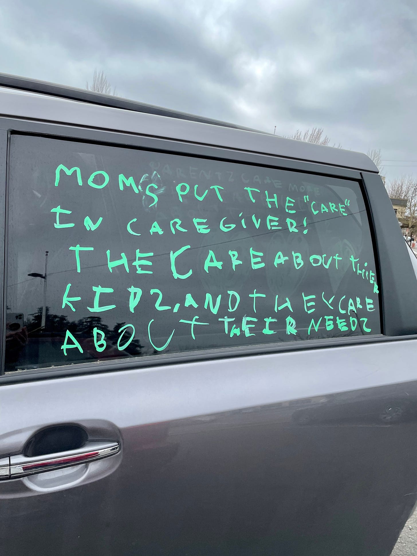 A child's writing in green marker on a minivan window reads "Moms put the 'care' in caregiver! They care about their kids and they care about their needs."