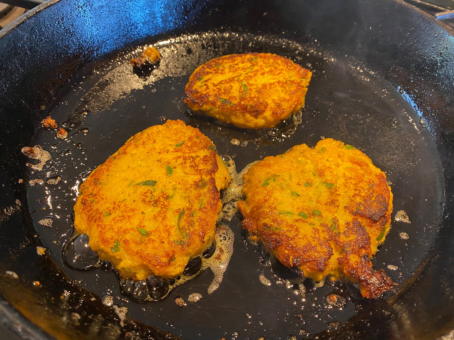 Three golden fritters sizzling in oil in a cast iron frying pan.