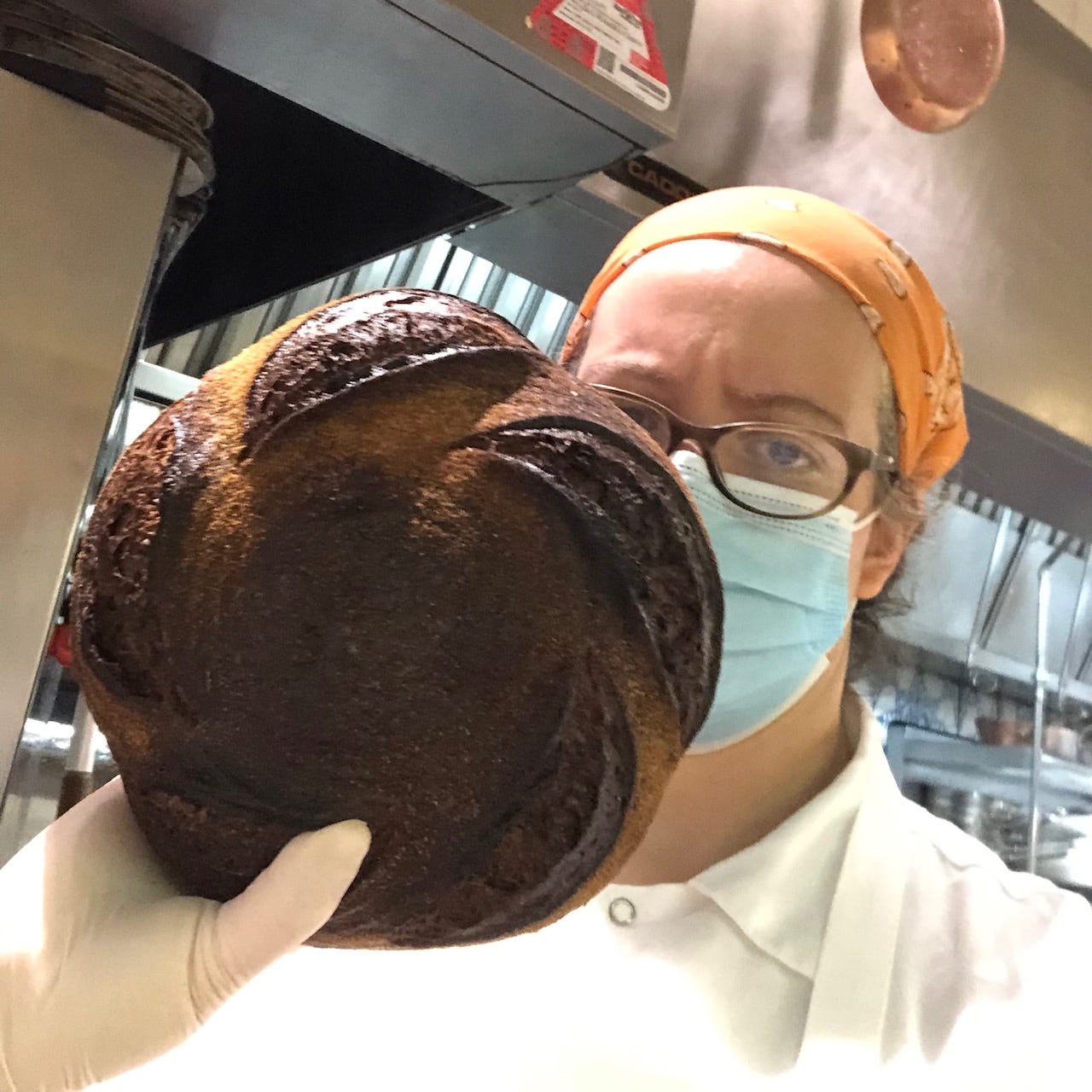 Me, wearing a medical mask, holding up a burned round loaf, and I look very upset with myself.