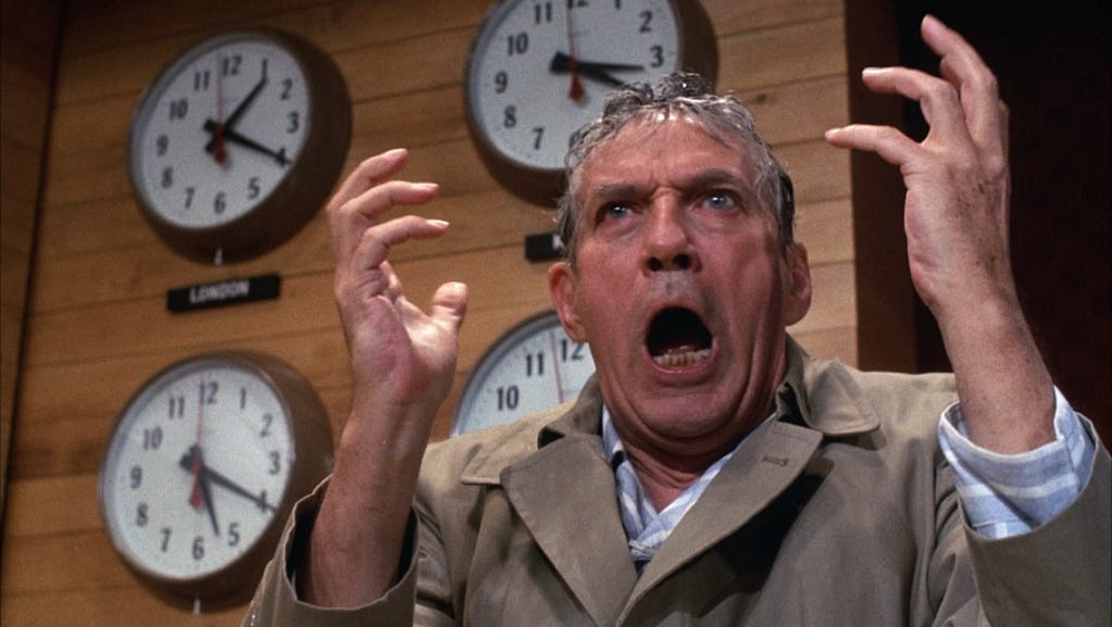 Howard Beale (Peter Finch) having a meltdown on live television in 'Network'. He is sweating, read faced, and is raising his hands, mouth open as if to yell.