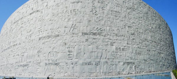 Parte externa da nova Biblioteca de Alexandria. Foto de xiquinhosilva/Flickr. Descrição de Imagem: a parede externa da biblioteca é feita de pedras brancas, com inscrições em diversos idiomas e alfabetos.