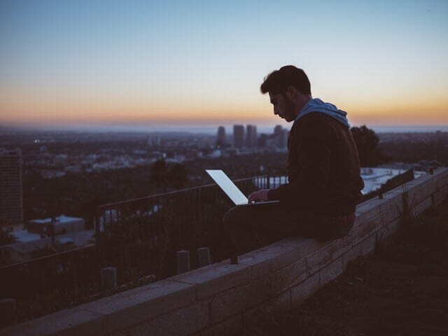 person working on laptop in the sunrise over a cityscape