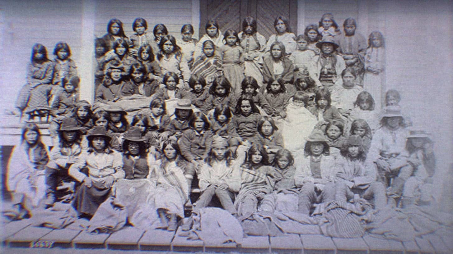 Ciricahua Apaches at the Carlisle Indian School. Children and adults sit on the porch of the school. Ciricahua Apaches at the Carlisle Indian School. Children and adults sit on the porch of the school.