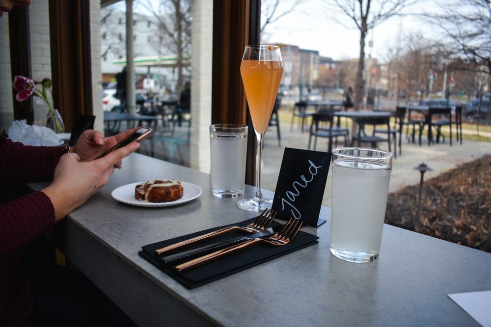 person holding smartphone near long-stem drinking glass