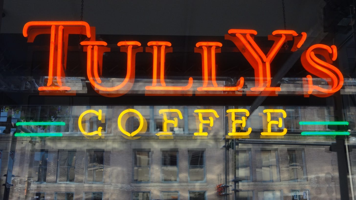 A neon Tully's Coffee seen through a window with the street reflected on top