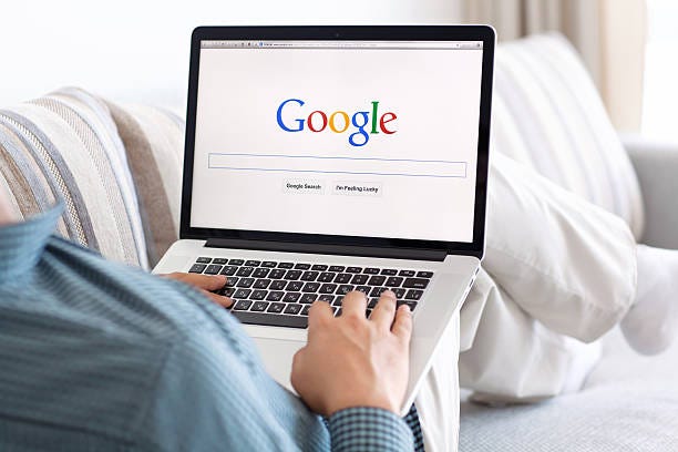 a businessman in a blue shirt googles on a laptop while reclining on a white couch