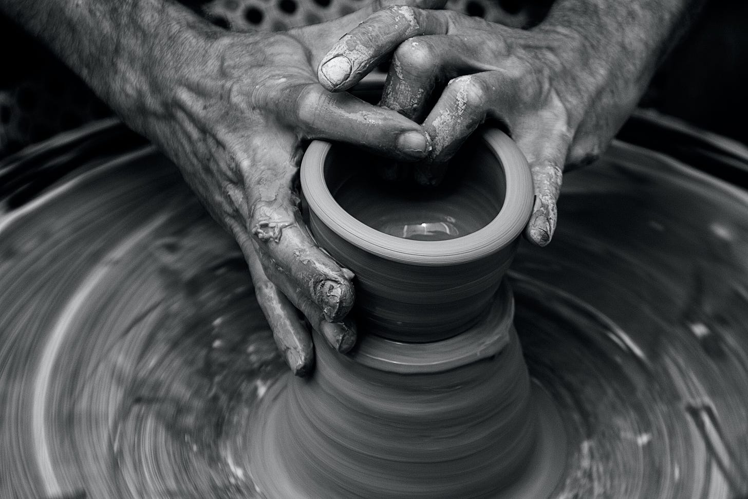 clay covered hands molding a cup on a throwing wheel