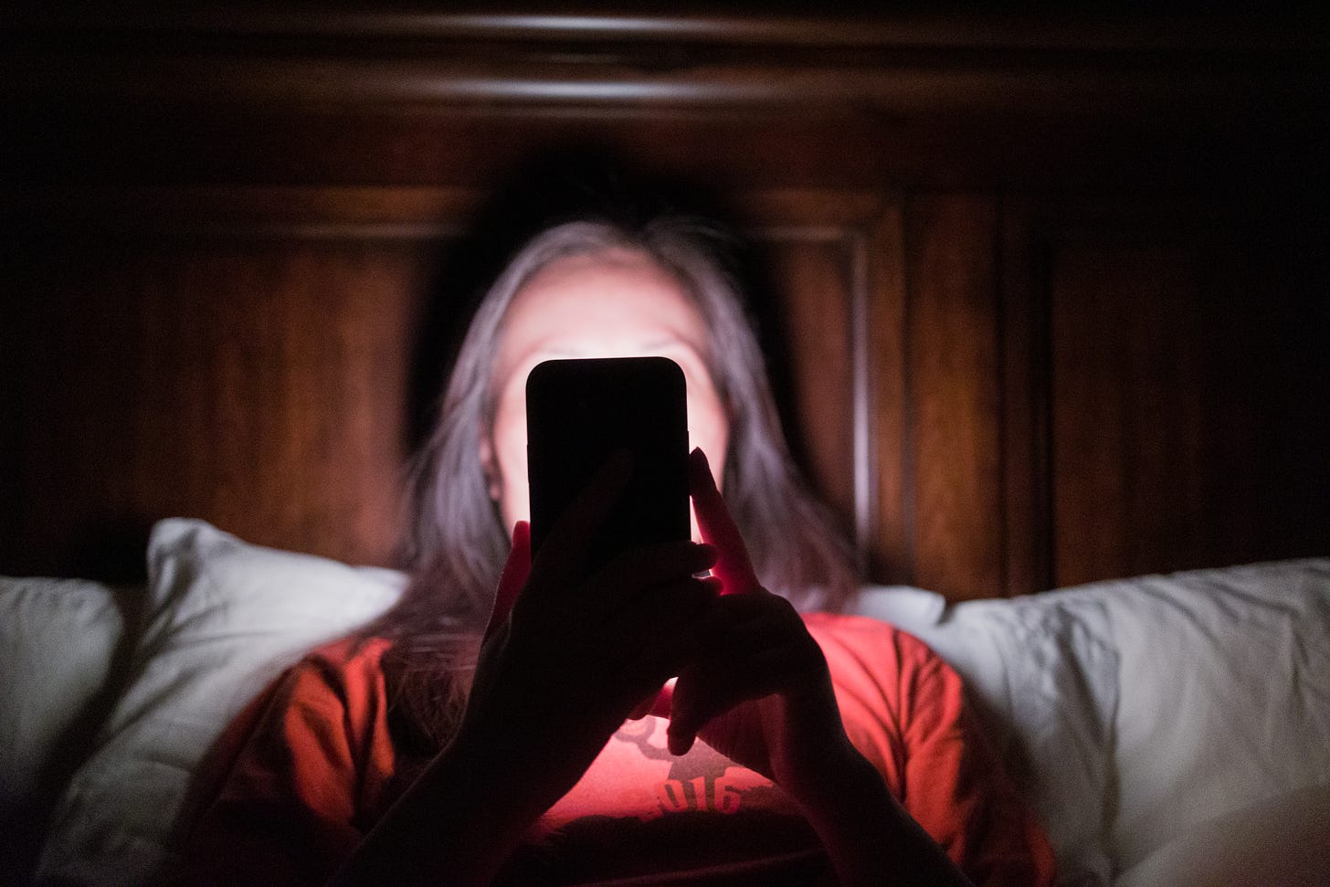 person looking at their phone in bed propped against white pillows