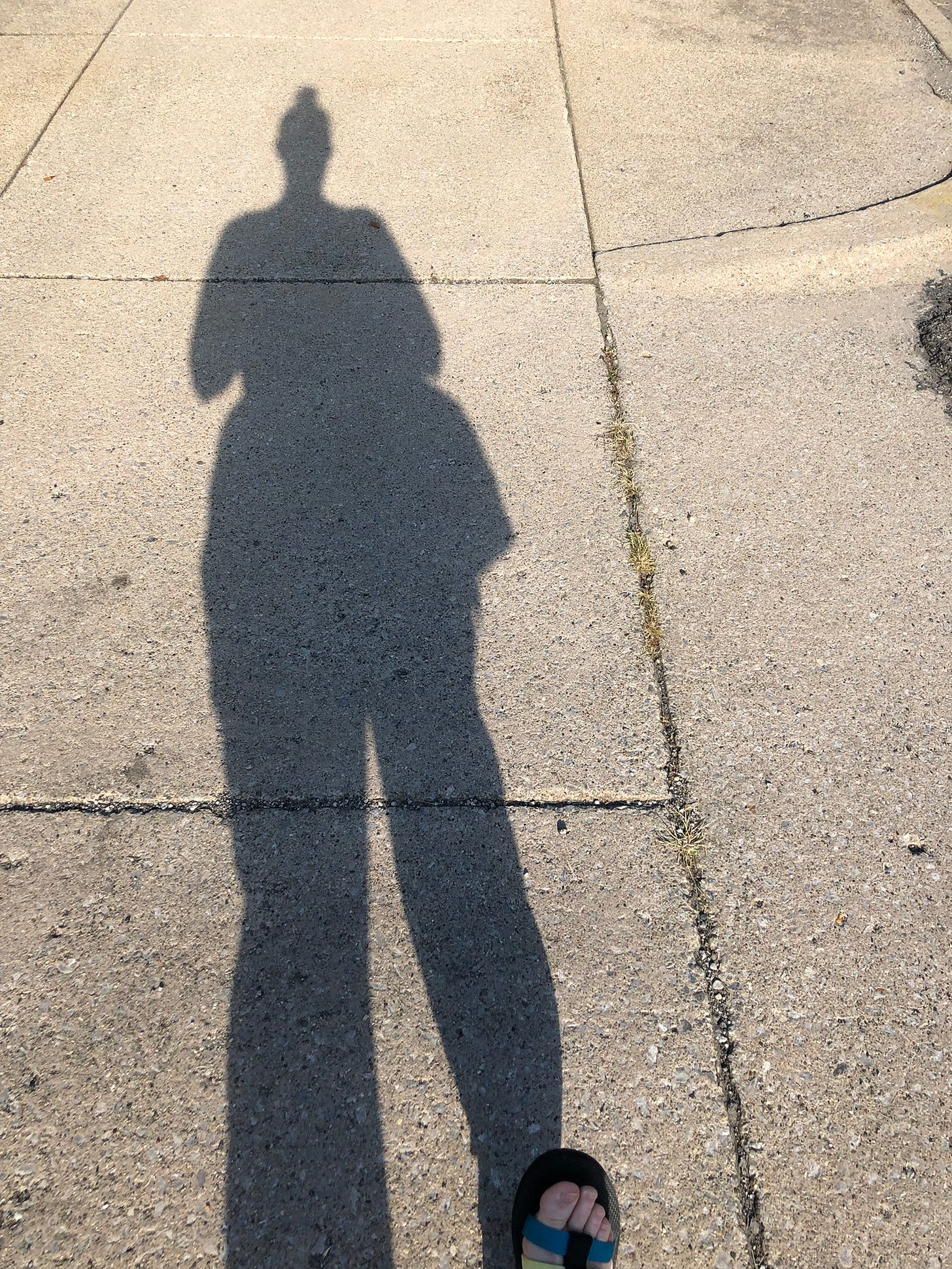 the shadow of a person elongated onto a segmented sidewalk
