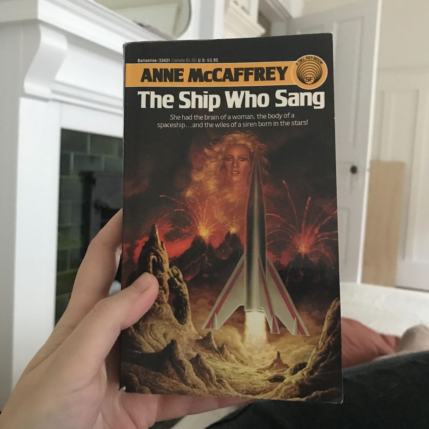 My hand holding a paperback copy of Anne McCaffrey’s The Ship Who Sang.
