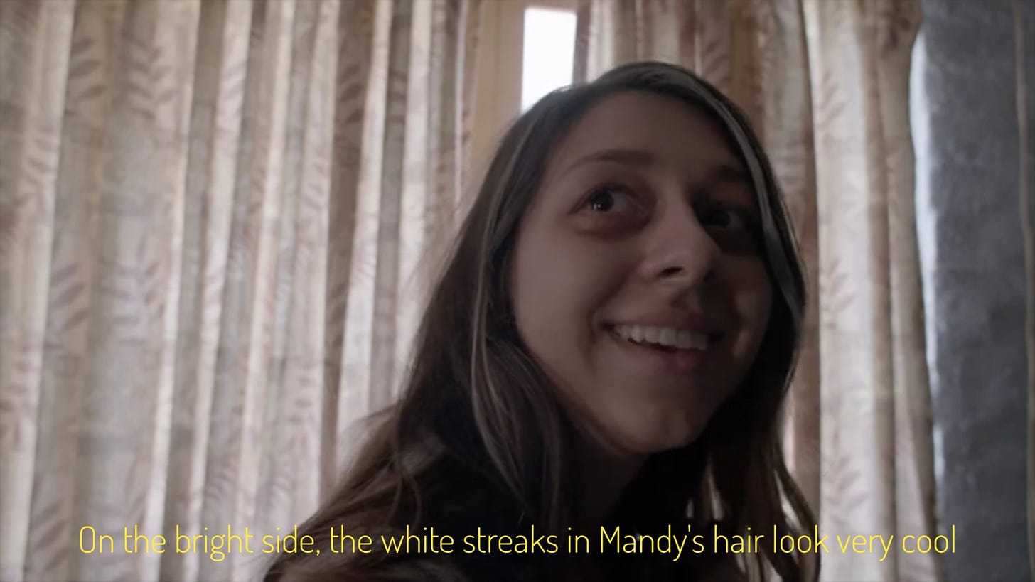 Mandy, who looks very tired, smiling in an unhinged way, captioned "On the bright side, the white streaks in Mandy's hair look very cool"
