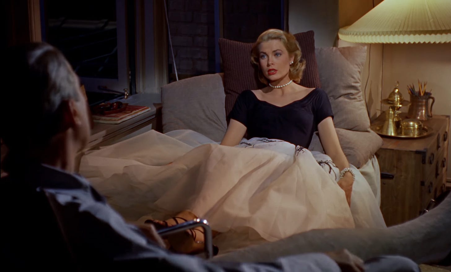 Jimmy Stewart (left) and Grace Kelly (right) sitting and conversing with one another in REAR WINDOW