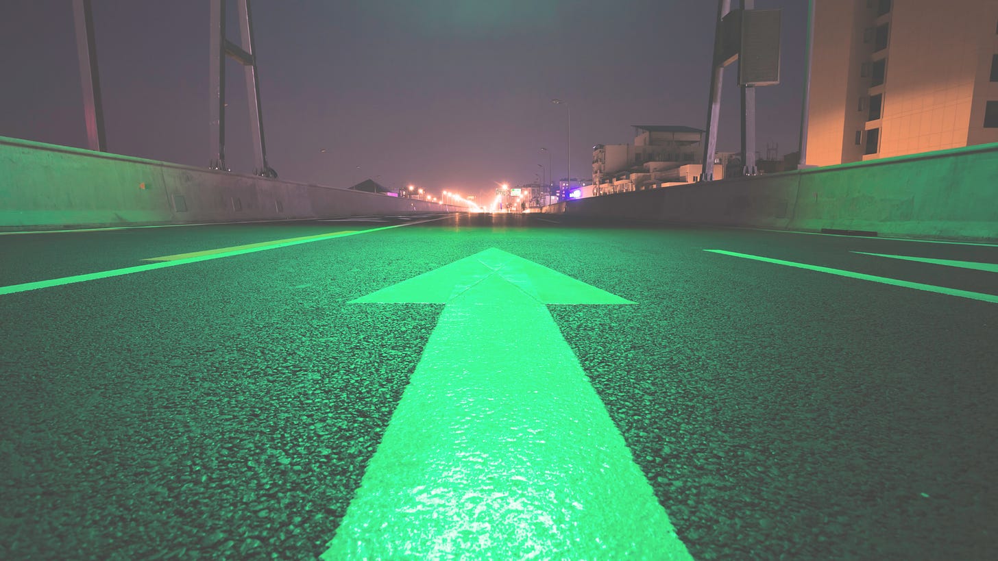 a green-lit road with an arrow pointing straight ahead