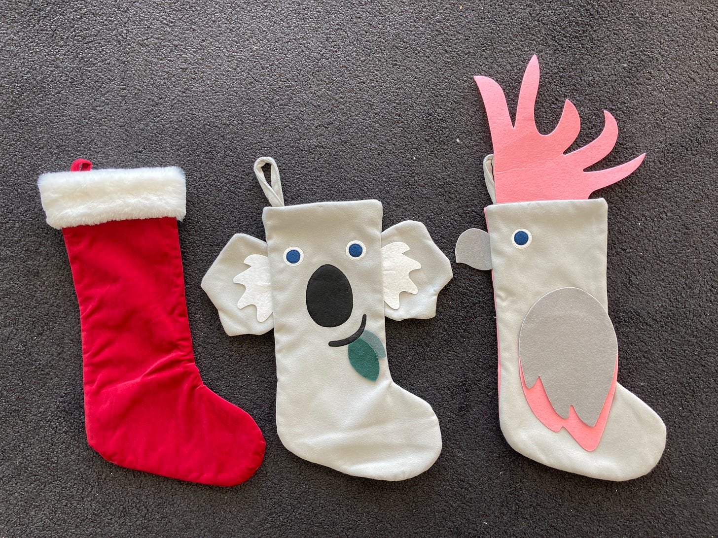 A picture of our Christmas stockings. One traditional red velvet and fur, one with a koala face and ears, and one pink cockatoo with a giant pink comb.