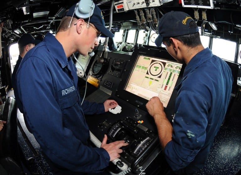 Navy personnel looking at a screen with data and guages. Below the sceen are some hardware controls