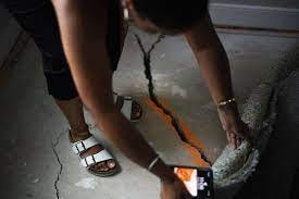 Black woman using orange paint and cell phone to document crack in concrete floor