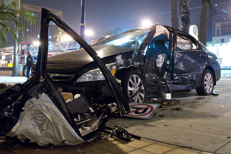 a wrecked car by the side of a road, with the side caved in following some sort of collision. the door has been removed