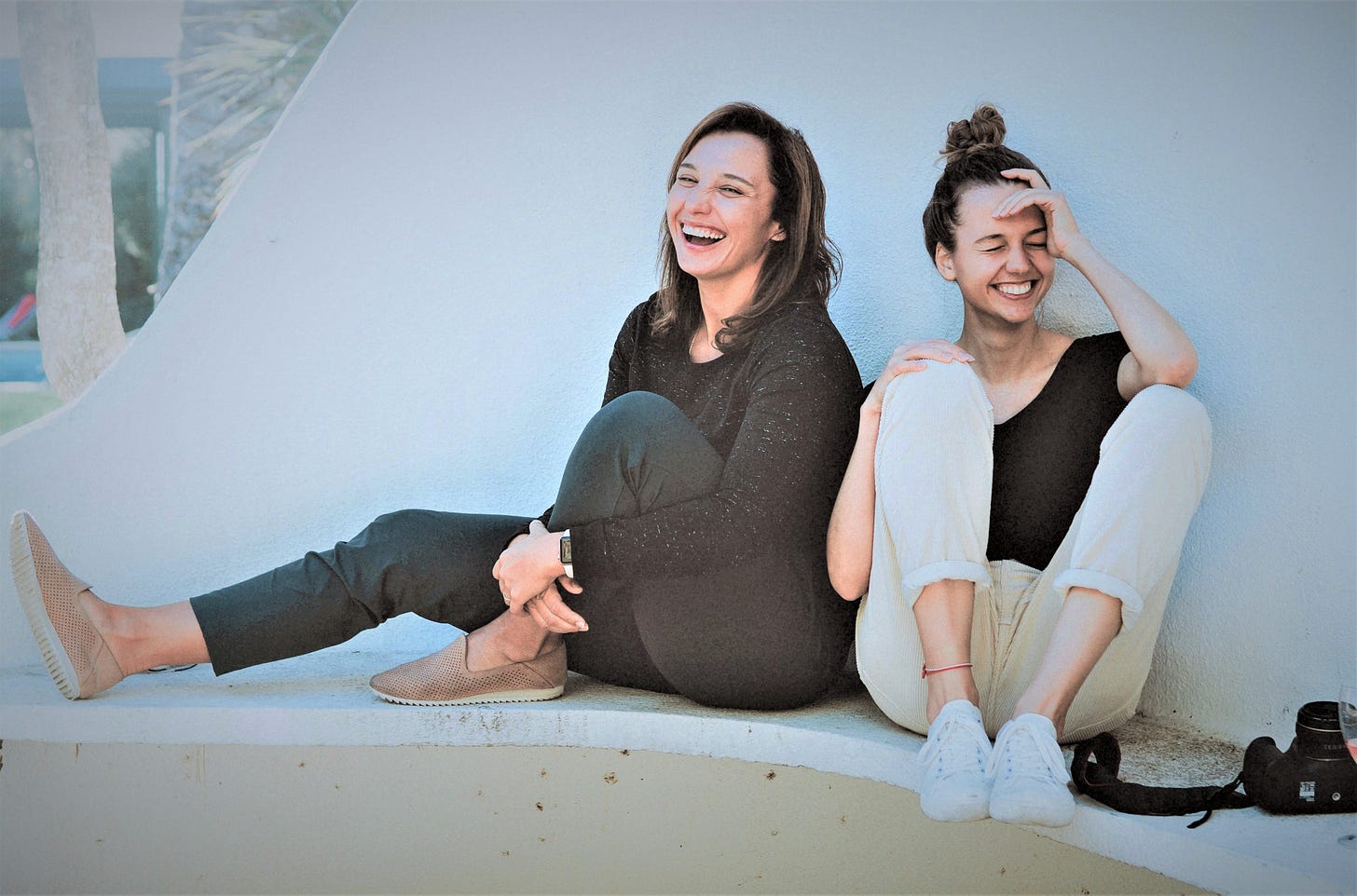 Two laughing girls sitting on white concrete bench