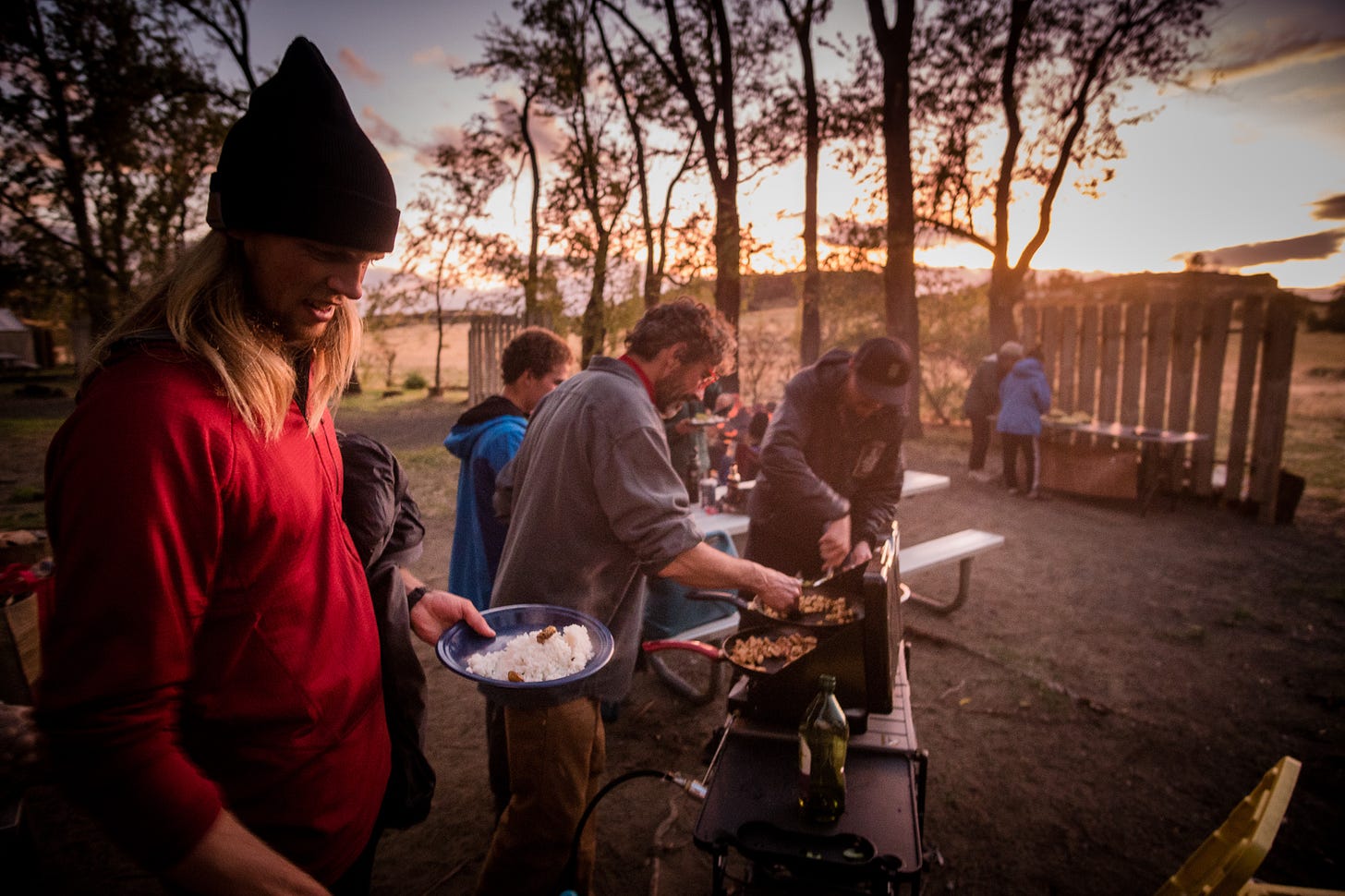 At sunset, people gather around a stove at a campground