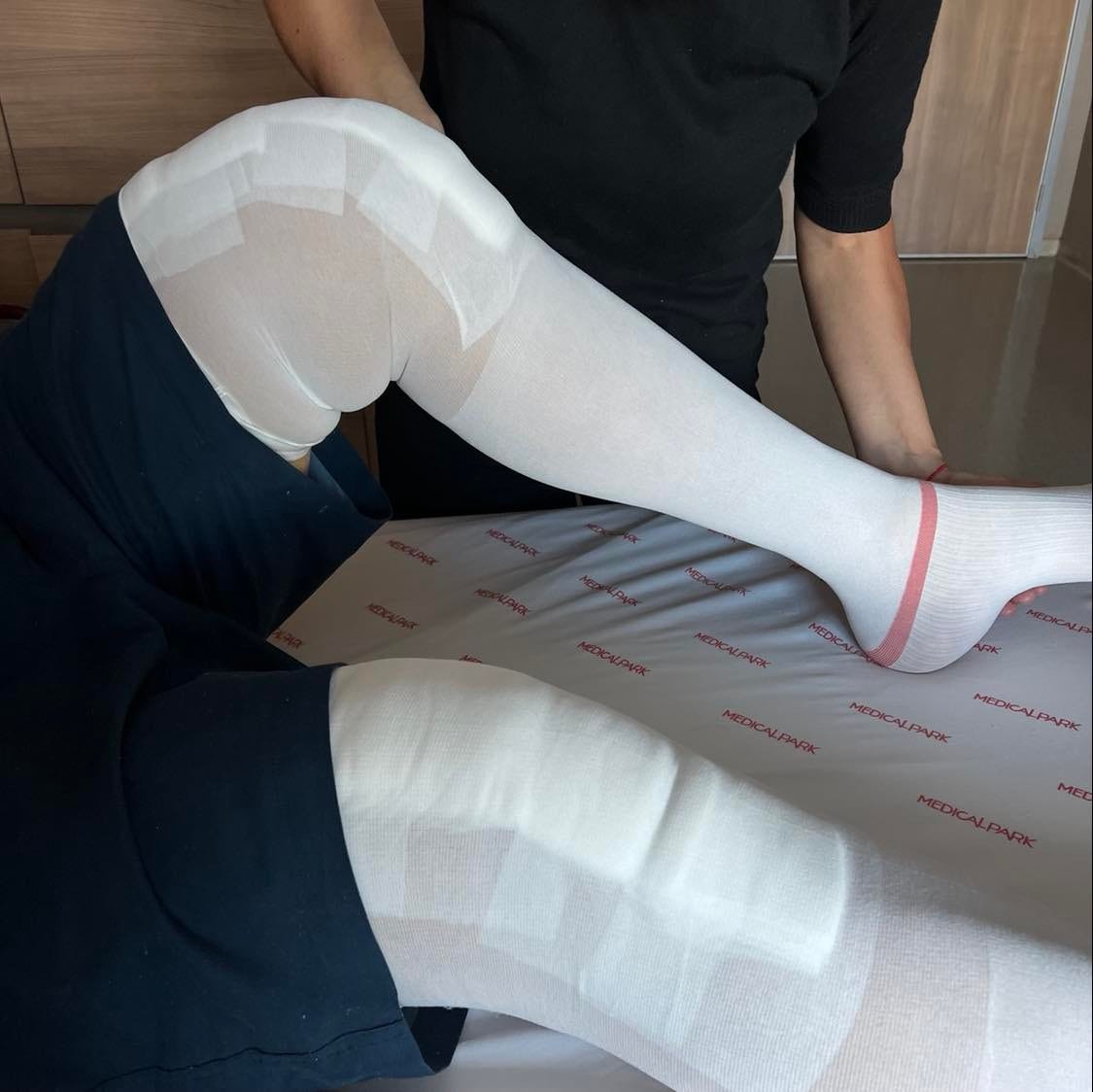 A close up of Tom's knees with bandages and compression socks on his legs. A physical therapist is helping with his physical therapy. 