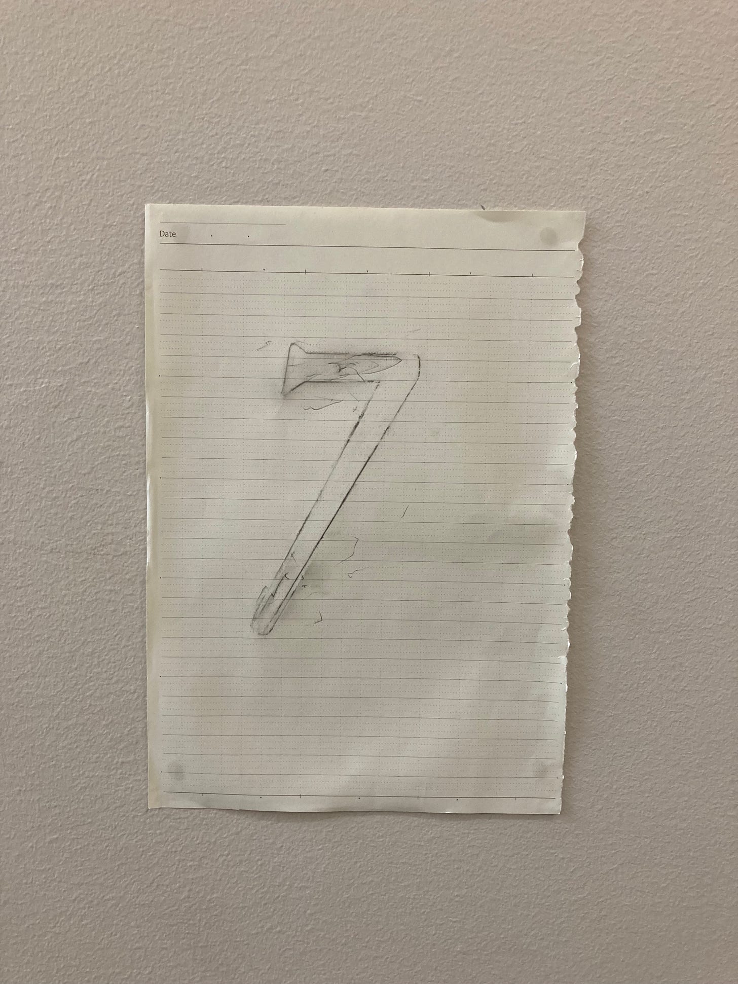 A lined piece of paper with the word "date" in the upper left-hand corner, hangs on a beige wall. The number 7 is outlined in pencil on the paper.