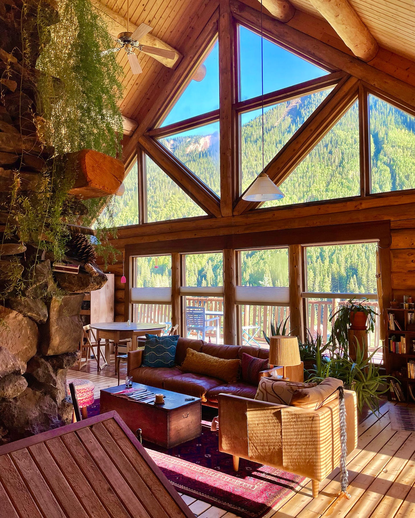 a cabin with a large window view of green trees and a mountain ridge line