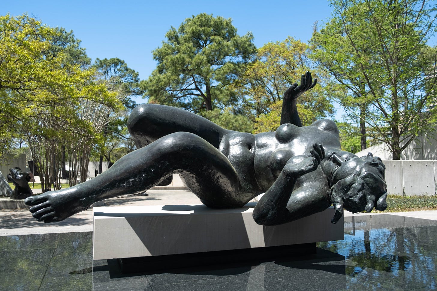 A reclining bronze nude,  Aristide Maillol’s La Rivière, set against green leafy trees in the in the sculpture garden at The Museum of Fine Arts, Houston. April 3, 2022.  
