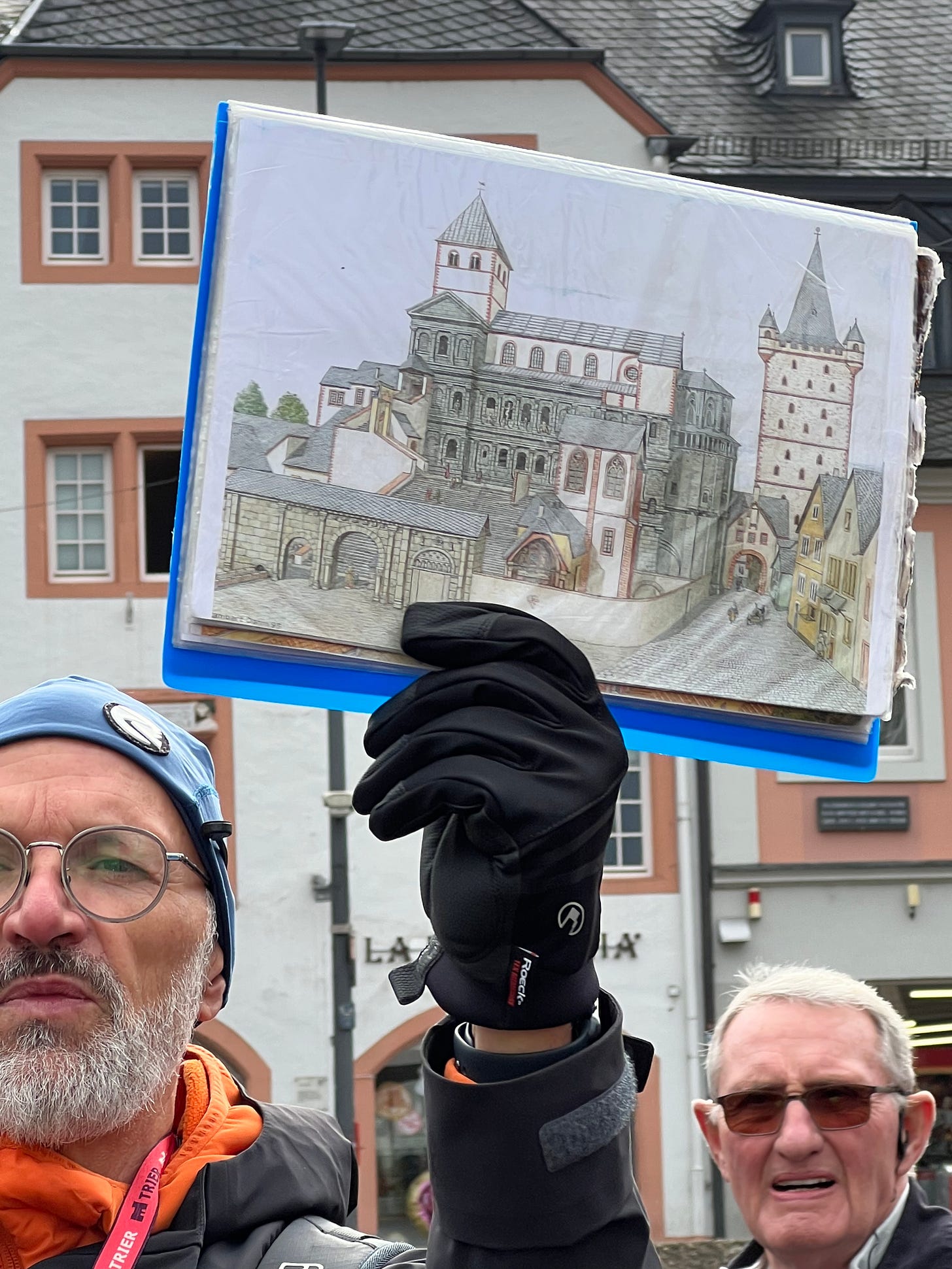 a man holding up an illustration of the porta nigra that shows how it was rebuilt as a church