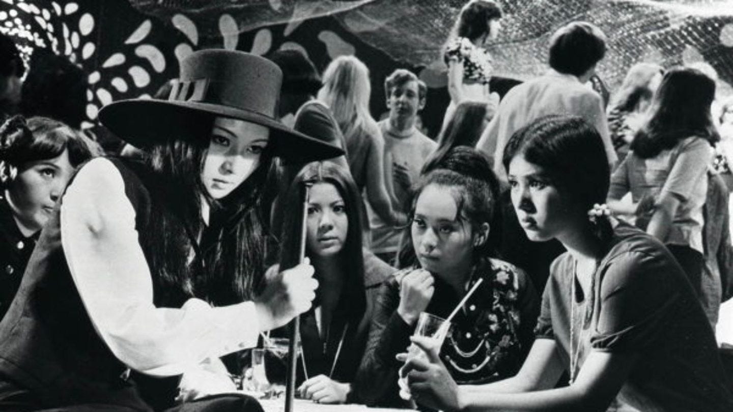 Film still from Stray Cat Rock. A badass girl gang gathers around a table.