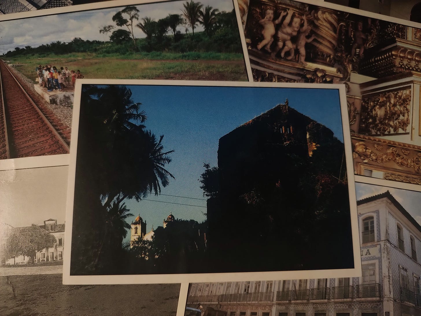 cartão postal com foto colorida de silhuetas de ávores e de ruínas de palacetes. ao fundo, duas torres de uma igreja católica.