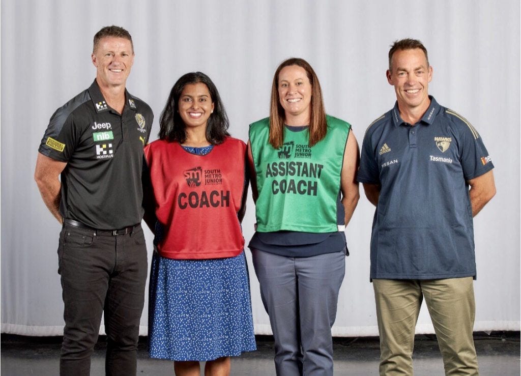 Image is a colour photograph of four people. From left to right, Richmond AFLM coach Damien Hardwick, WCA co-founder Aish Ravi, WCA co-founder Julia Hay, and Hawthorn AFLM coach Alistair Clarkson. 
