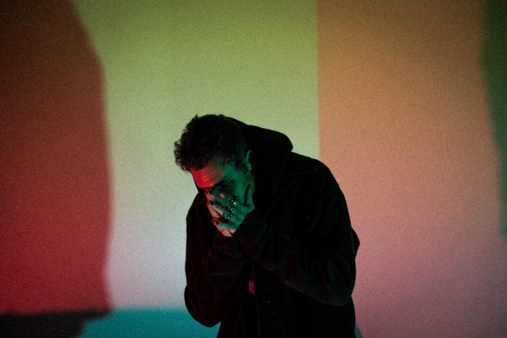 cøzybøy holding his hands to his face, posing in the center of a moody photo with red, green, orange and pink gradients.