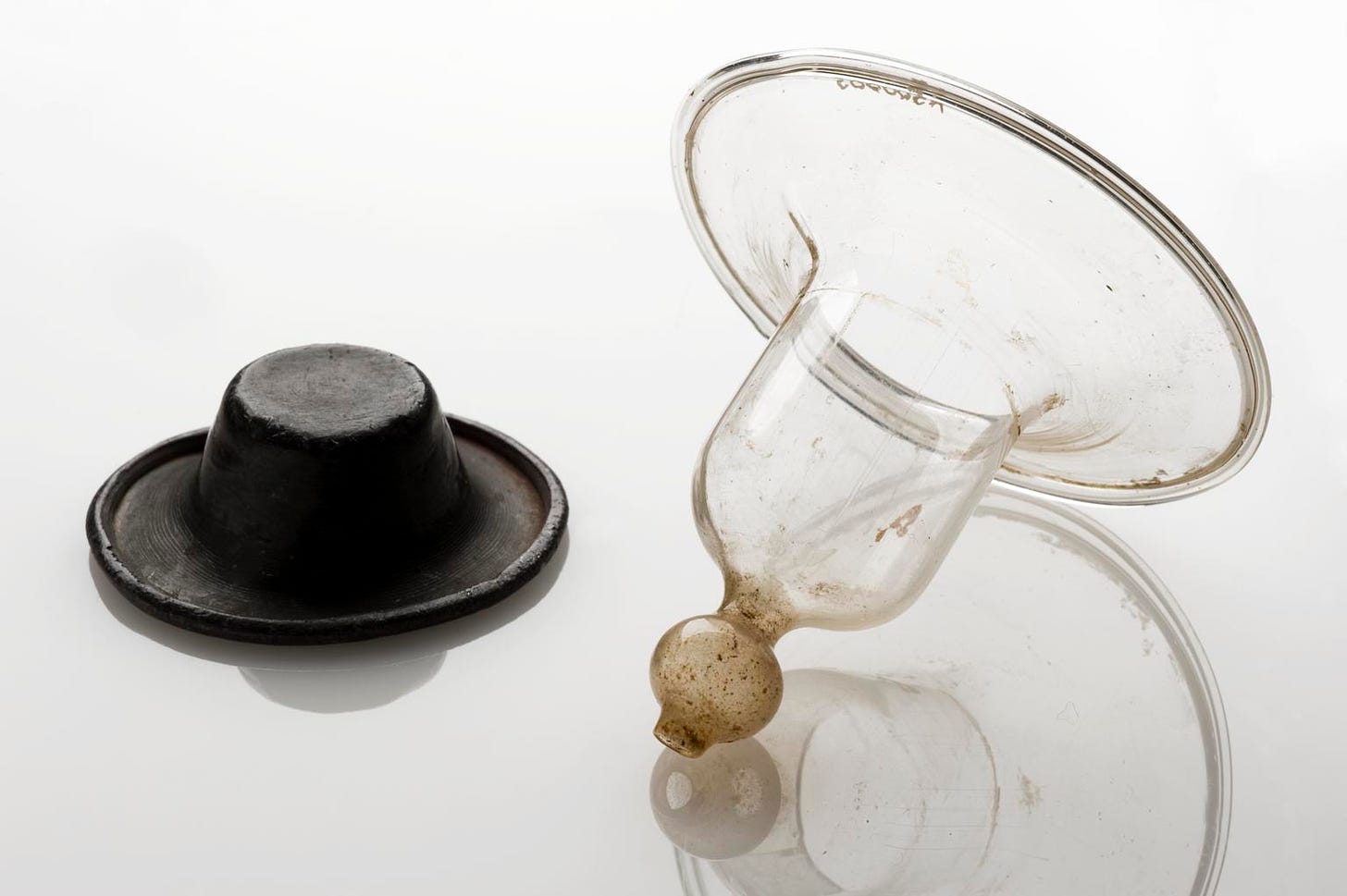 on left, a dark lead nipple shield, on right, a glass nipple shield shaped like a bell