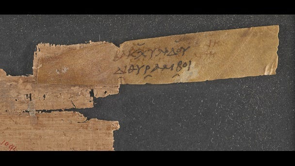 A small fragment of a 2nd-century papyrus scroll, with an attached parchment sillybos, or label, inscribed with the title of a work by Bacchylides. 
