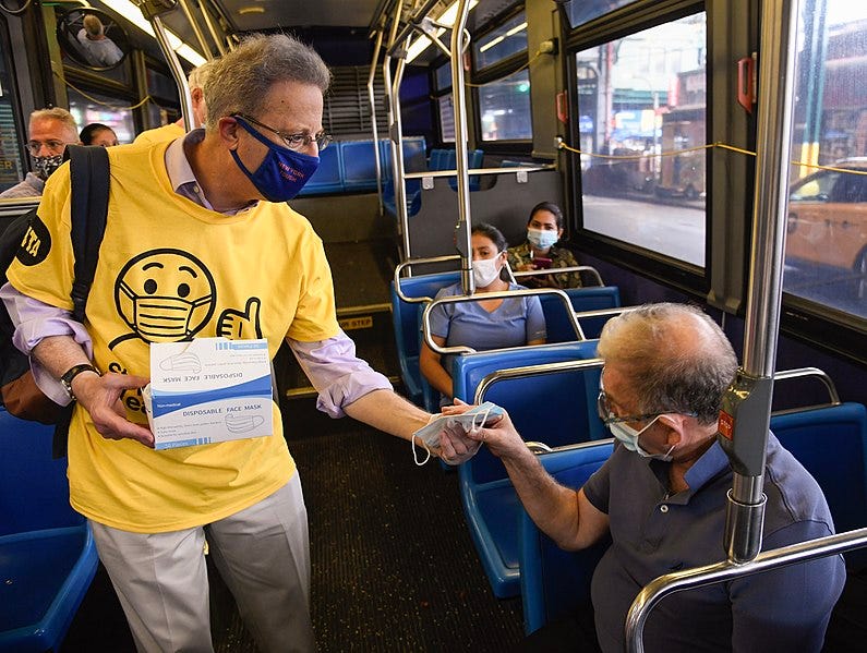 A man is handing out masks to passengers on a local bus