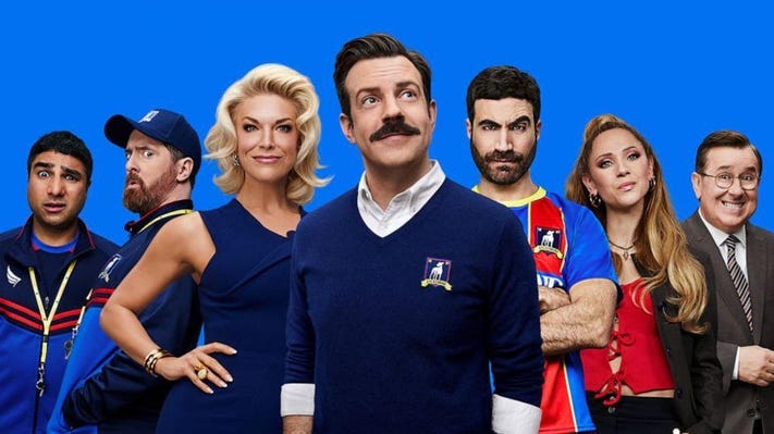 Promo photo for Ted Lasso featuring seven of the cast members with Ted front and centre