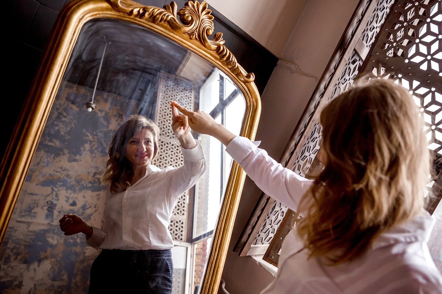 A woman smiles as she traces her reflection in a mirror.