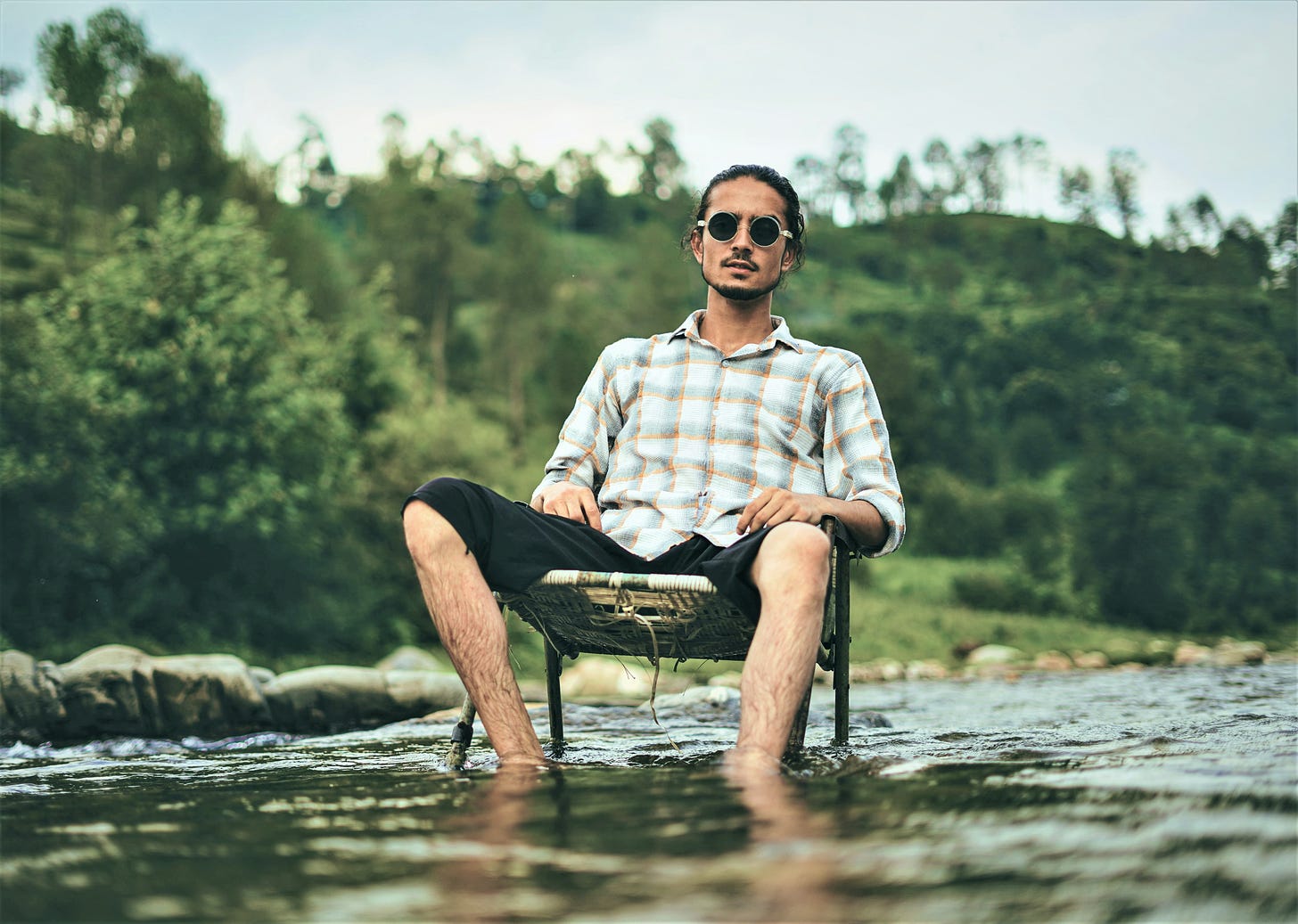 man wearing sunglasses and plaid shirt sitting in lawn chair in middle of a river