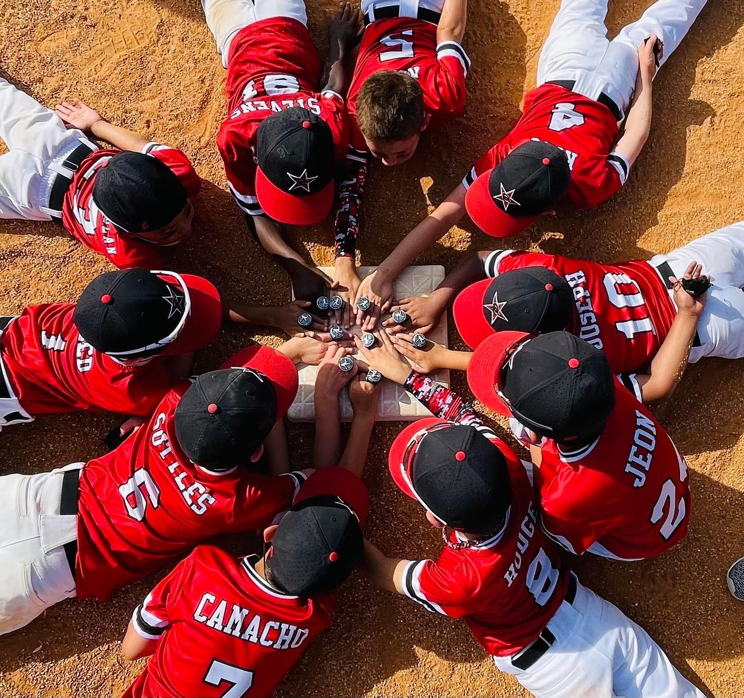 A group of youth baseball players placing their hands on a base while wearing championship rings