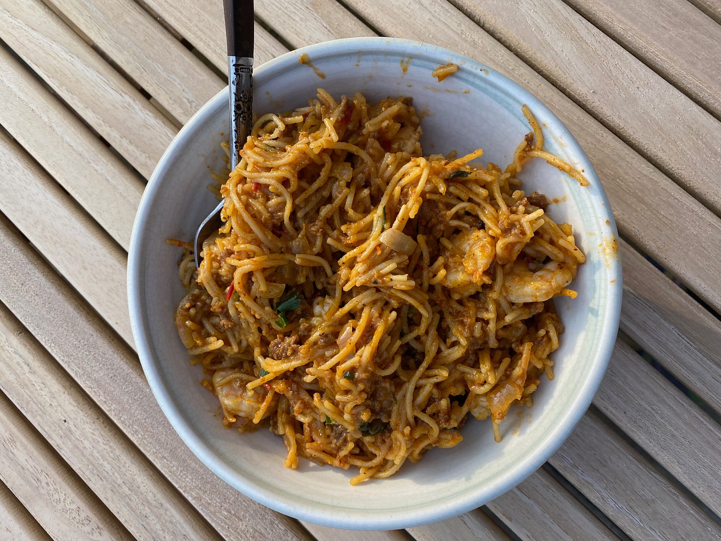 A ceramic bowl of angel hair pasta in a spicy red sauce sits on a wooden outdoor table.