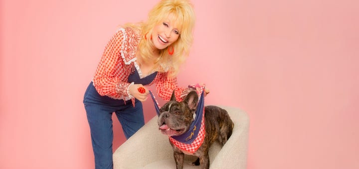 Dolly parton posing with a French bulldog, both are wearing red and white gingham