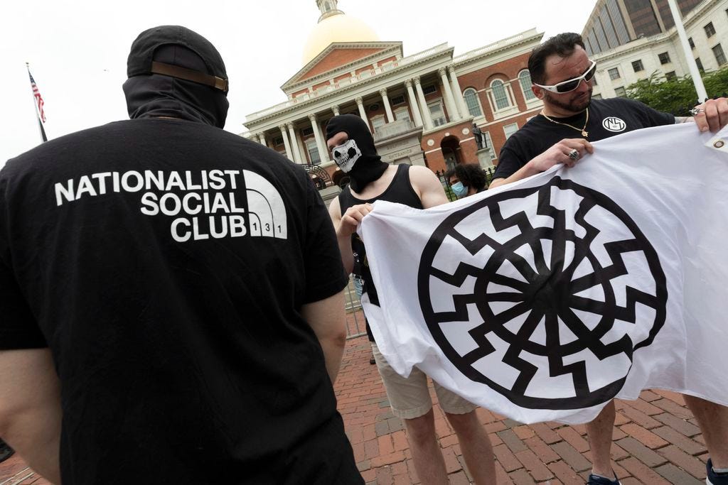 Members of the Nationalist Social Club held a "sonnenrad" flag at a June rally in front of the State House.