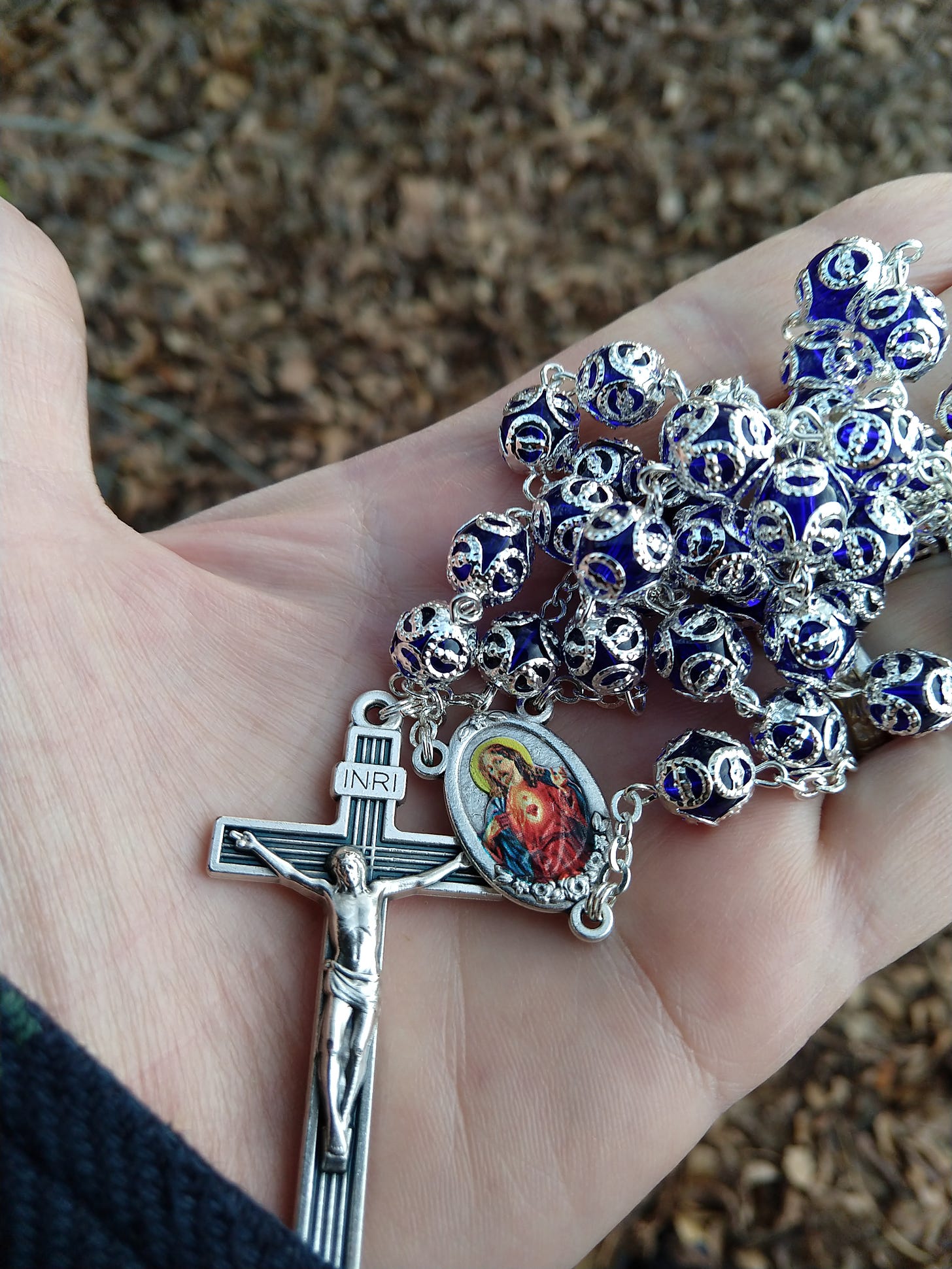 My hand holding a blue rosary with silver metalwork and a sacred heart medallion